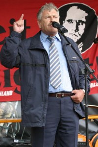 Udo Voigt, former leader of the NPD, standing in front of a banner depicting Nazi leader Rudolf Hess. Hess, who died in prison in 1987, is considered a martyr by the NPD © Marek Peters Photo Agency | Wikimedia Commons