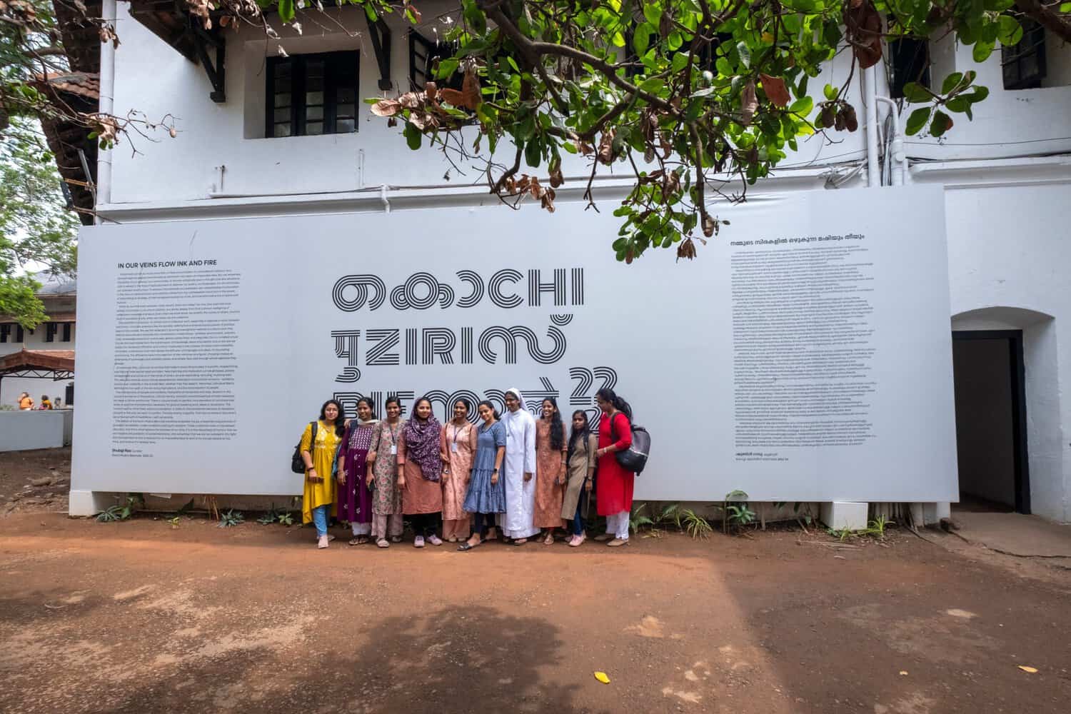 Visitors to the 2022–23 Kochi Muziris Biennale pose with wall text