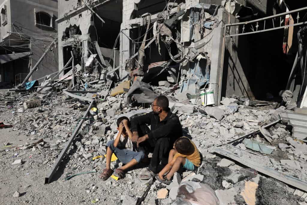 Photograph of Palestinian man and children sitting outside a house after an Israeli air strike, in the city of Rafah, south of the Gaza Strip, on October 12 2023.