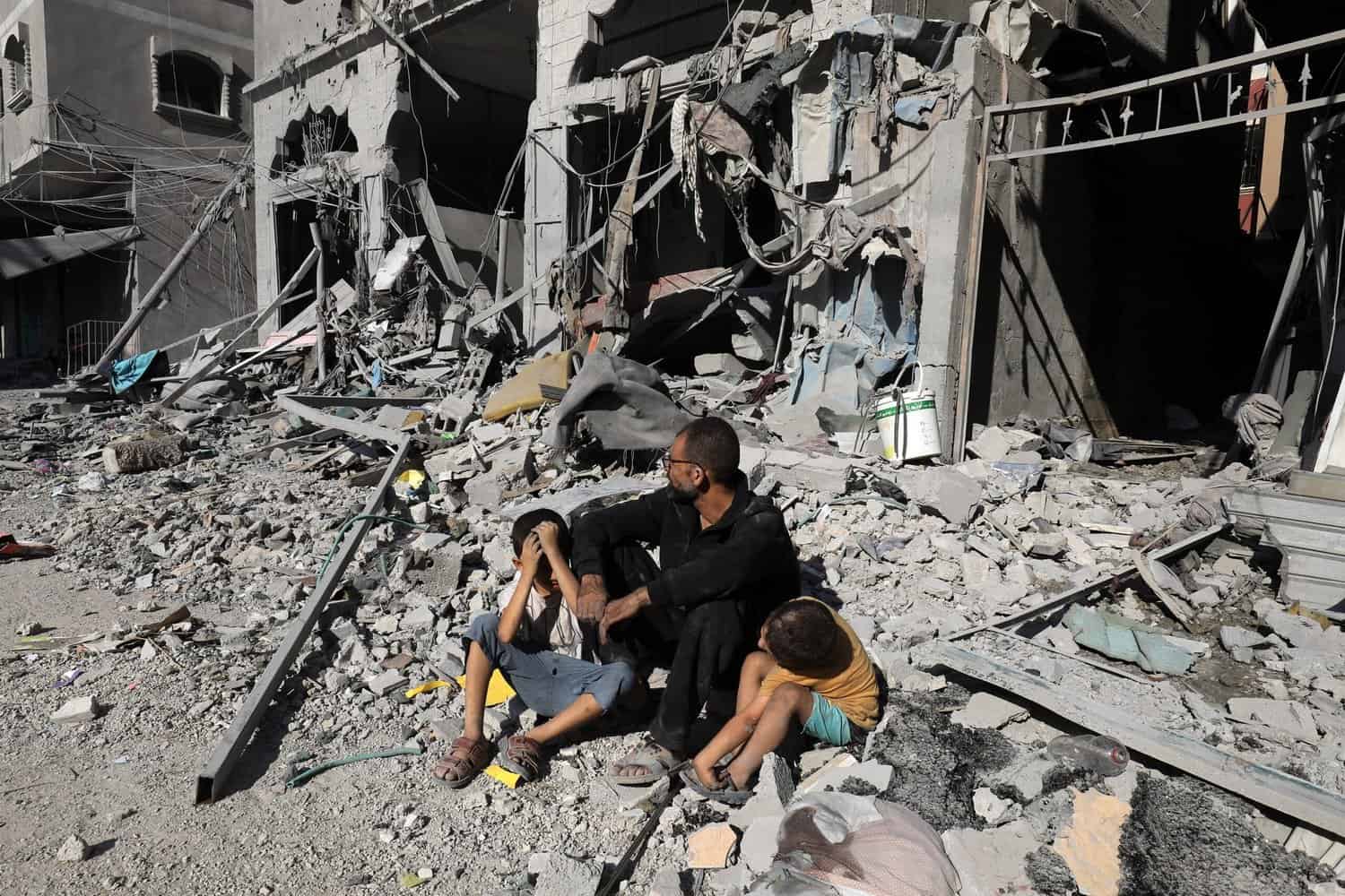 Photograph of Palestinian man and children sitting outside a house after an Israeli air strike, in the city of Rafah, south of the Gaza Strip, on October 12 2023.