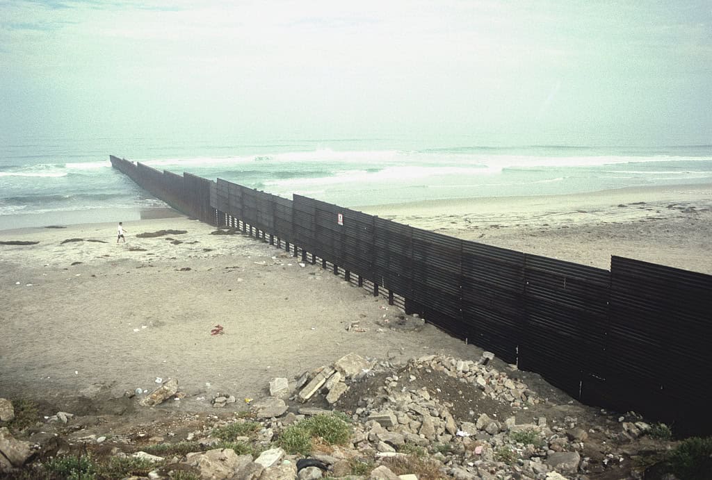 Man walks toward border fence on beach stretching into ocean