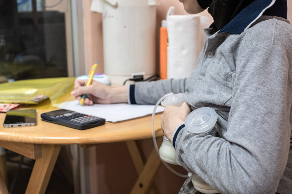 Parent writes at desk while using breast pump