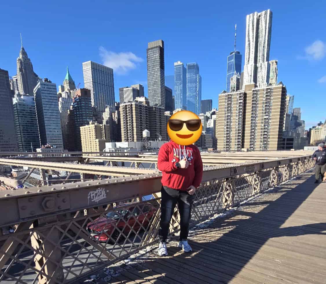 Figure on Brooklyn Bridge with face covered by emoji wearing sunglasses
