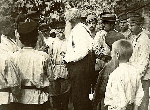 Black and white photograph of man with white beard talking to Russian peasants