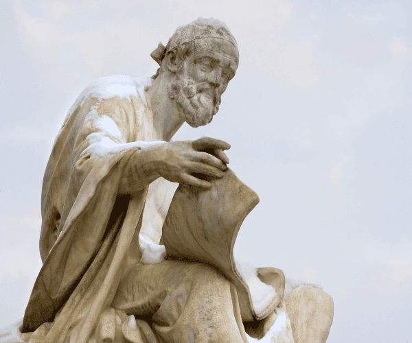 Color photograph of marble statue of Ancient Greek philosopher holding manuscript. There is some snow on the statue's shoulder and arm.