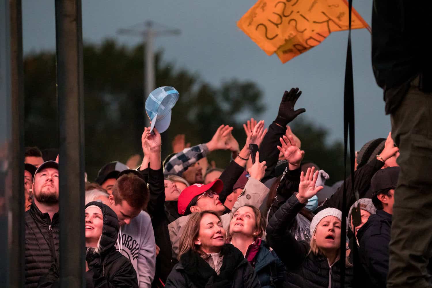 Crowd of people in winter clothes stand with their hands and faces raised in worship