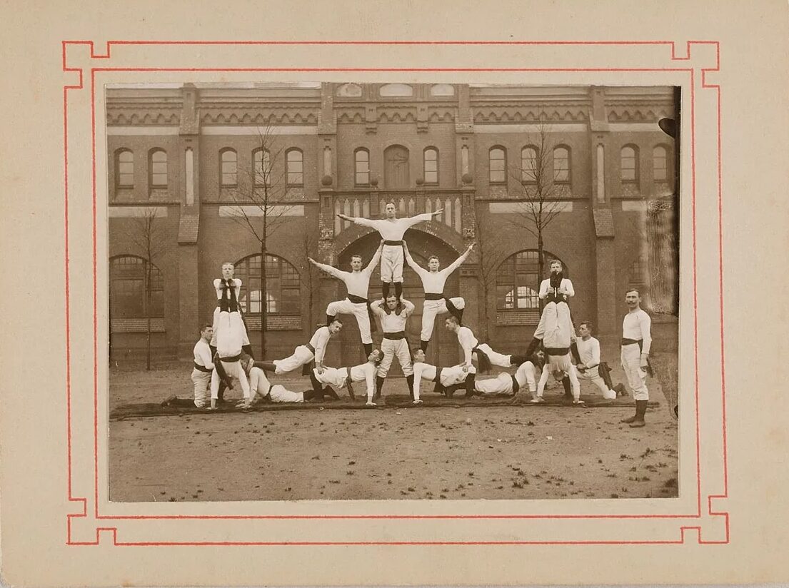Black and white photograph of men in twentieth-century white sporting outfits standing in acrobatic formation
