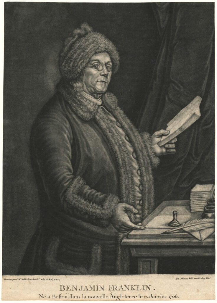 Black and white mezzotint on paper of man in spectacles and fur hat holding a book in his left hand. His right hand gestures to a quill and piece of paper on the desk in front of him