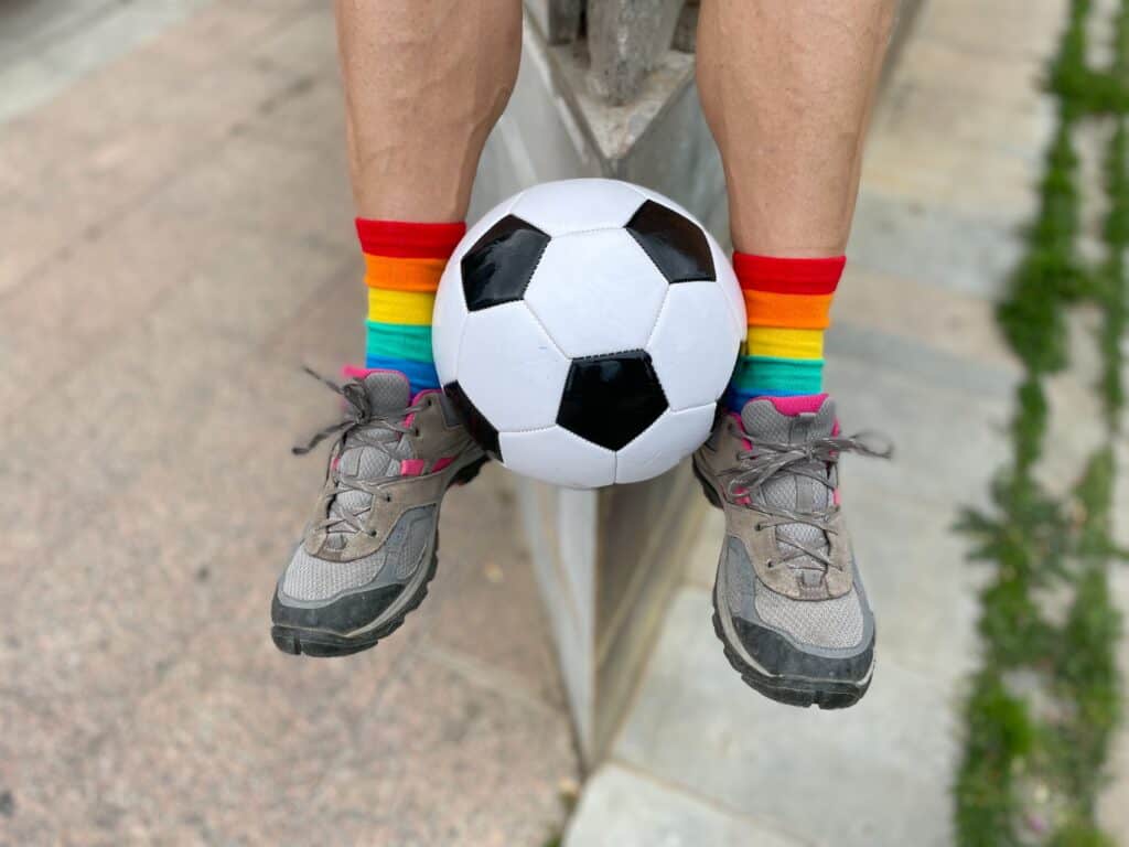 Soccer ball between two legs with socks with the color of the rainbow
