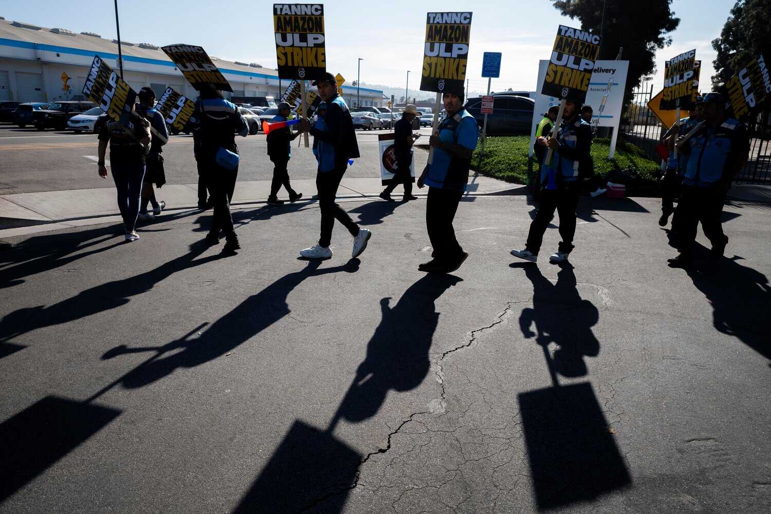 Photograph of protesters wearing blue amazon vests and holding signs marching in a picket line