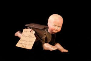 Photograph with black background of crawling white baby doll with realistic head and limbs and wooden mechanical body