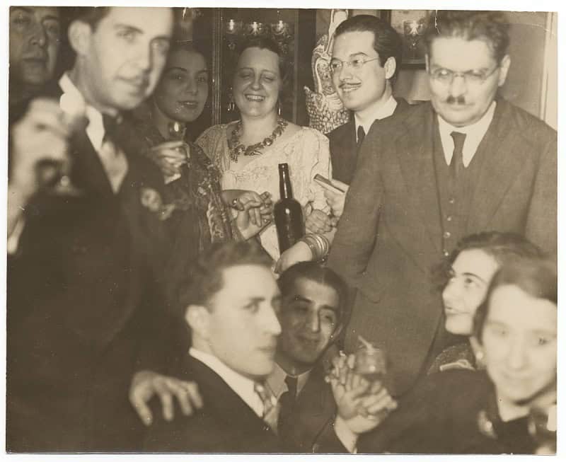 Black and white photograph of men and women in 1930s dress at a crowded social gathering