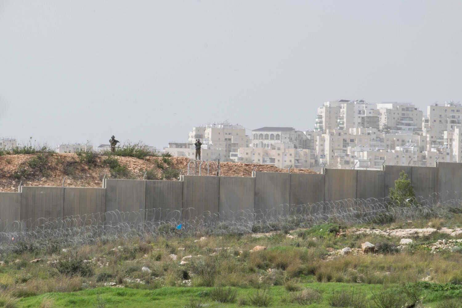 Two Israeli soldiers patrol along a concrete barrier in the West Bank