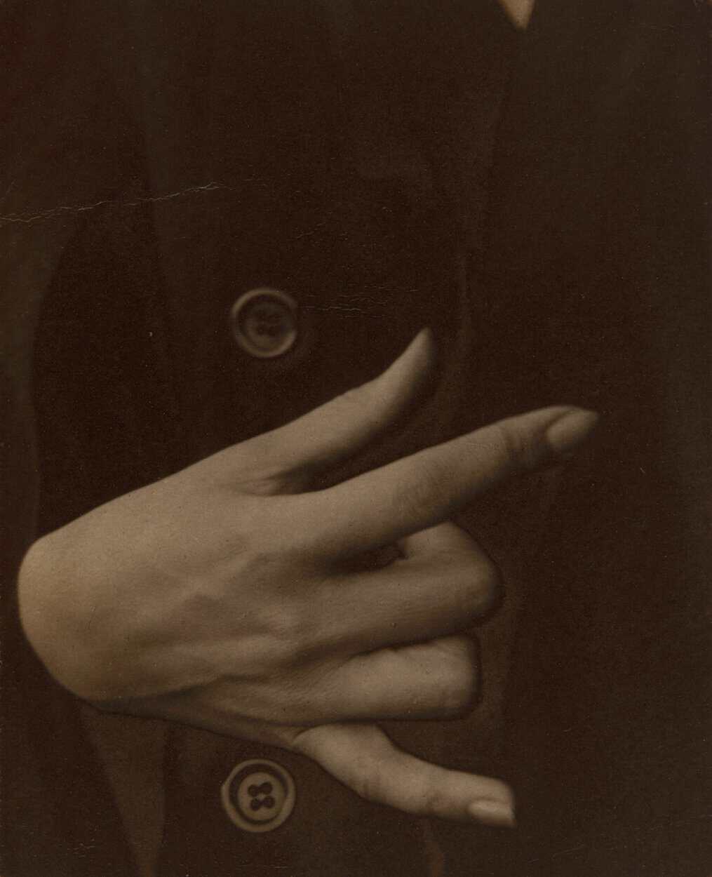 A cropped photo of Georgia O’Keefe’s hand, playing with the buttons on a coat