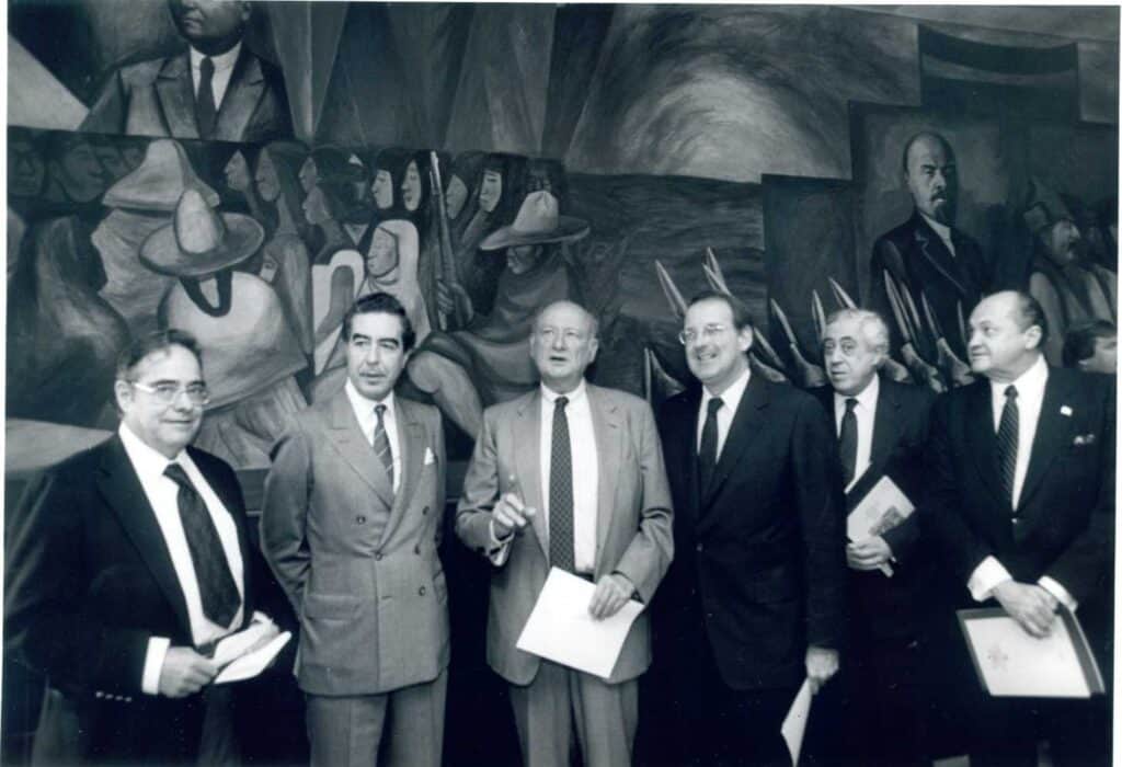 Black and white photo of men in suits standing in front of a mural