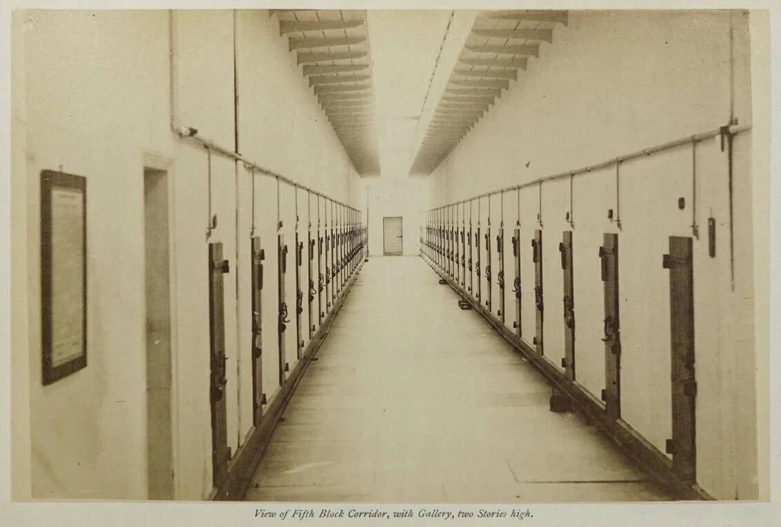 Black and white photo of a corridor of a prison block showing rows of locked doors