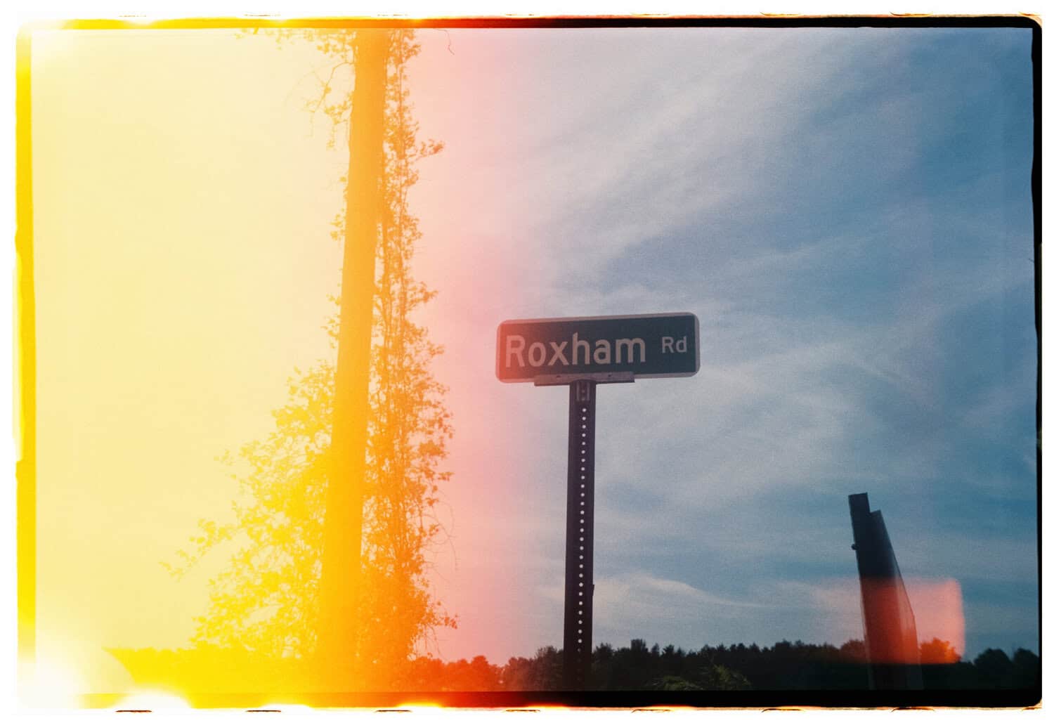 Film photograph with double exposure of yellow light over a sign saying "Roxham Rd"