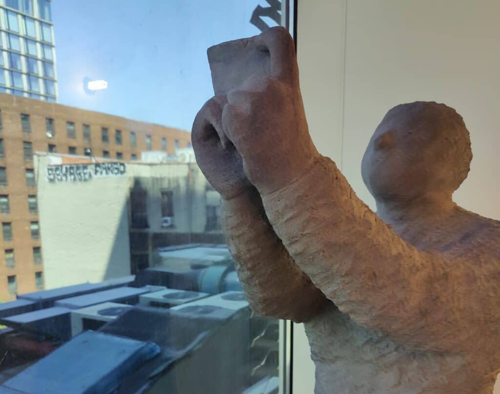 Photograph of clay figure holding up smartphone-shaped object in front of window