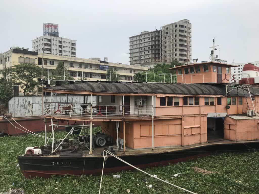 Photograph of a decaying orange paddle steamboat on the banks of the Buriganga River in Dhaka, Bangladesh.