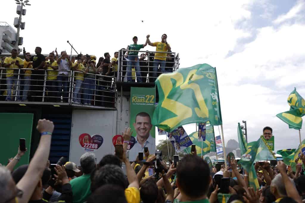 Flavio Bolsonaro addresses a crowd of supporters dressed in yellow and green and waving flags.